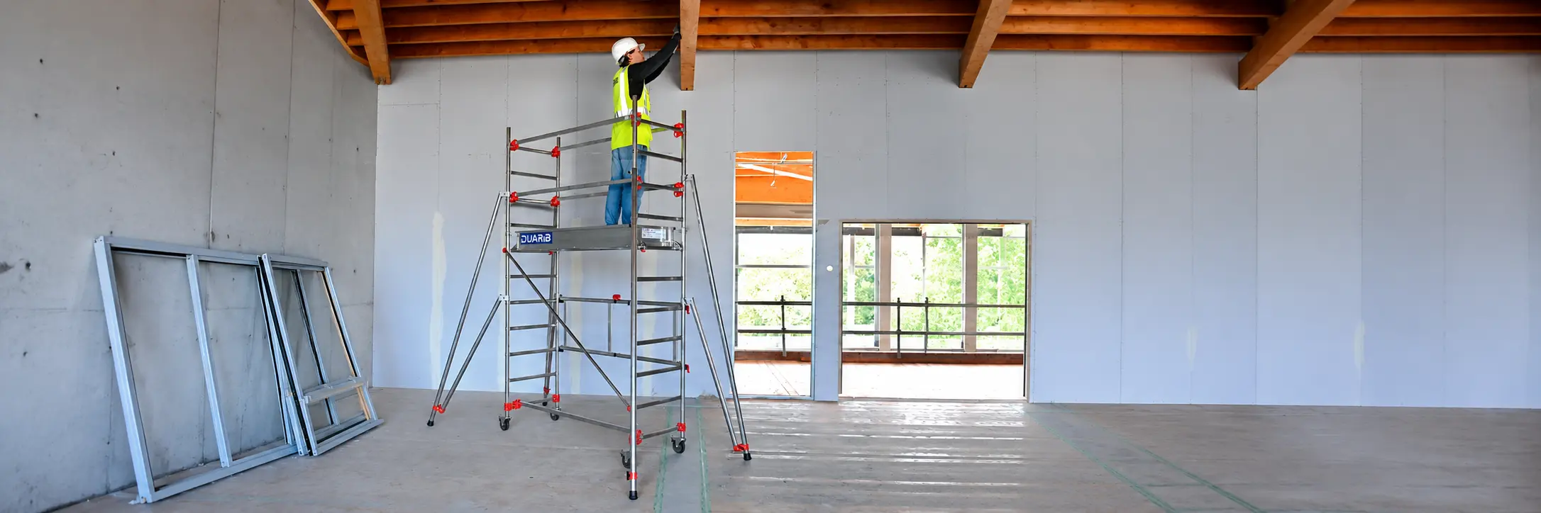 Échafaudage mobile avec un professionnel du bâtiment travaillant sous une charpente en bois
